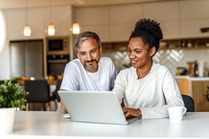 Husband and wife homeowners in kitchen using laptop to opt out of mortgage spam.