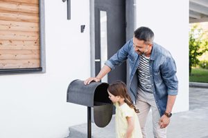 Smiling father and daughter checking their mailbox for mortgage mail. 