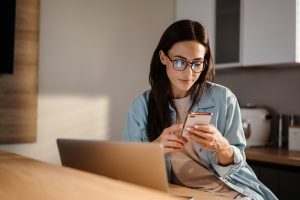 Fraud Prevention Banking in Boone County, MO - a brunette woman checks her phone while sitting next to her laptop 