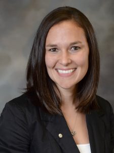 Janine Brinker, Director of Loan Operations - smiling headshot with dark blazer over white shirt, brunette hair, and gray background