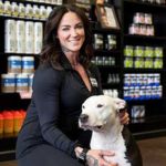 Business Banking Services client - Nutrishop owner poses with pet dog in front of health and fitness products