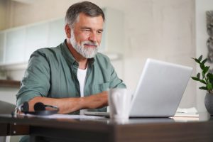 Fraud Prevention in Columbia, MO | Handsome mature man in casual suit sitting at the table in home office and thinking on his work, when looking at laptop screen