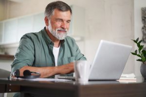 Fraud Prevention at Local Bank in Columbia, Missouri | Handsome mature man in casual suit sitting at the table in home office and working at laptop